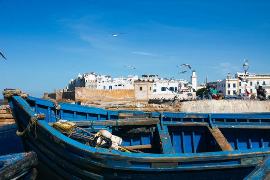 A blue fishing boat in Essaouira harbor with white-walled medina in the background