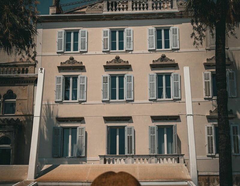 SJ in a straw hat looks at a beige building with multiple windows and balconies under a clear, dark sky in Split Croatia.